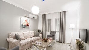 A modern living room with a sofa, armchair, coffee table, and a flat-screen TV. - Rodina Suites (Kusadasi)