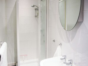 A bathroom with a shower, a sink, a mirror, and a towel rack.