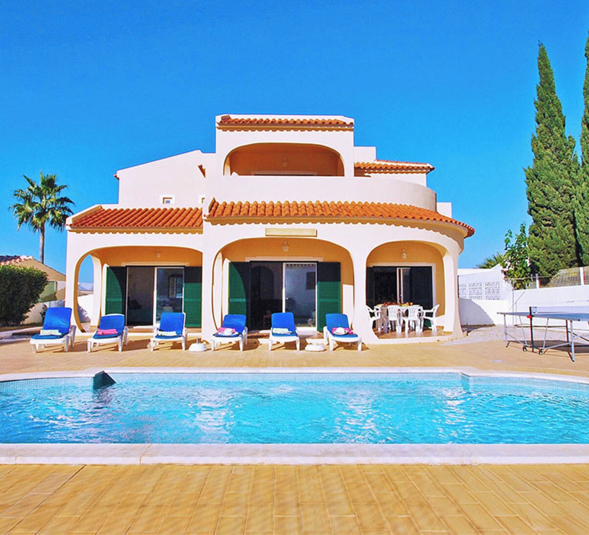 A resort with a swimming pool, lounge chairs, and a covered area with tables.