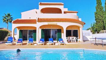 A resort with a swimming pool, lounge chairs, and a covered area with tables.