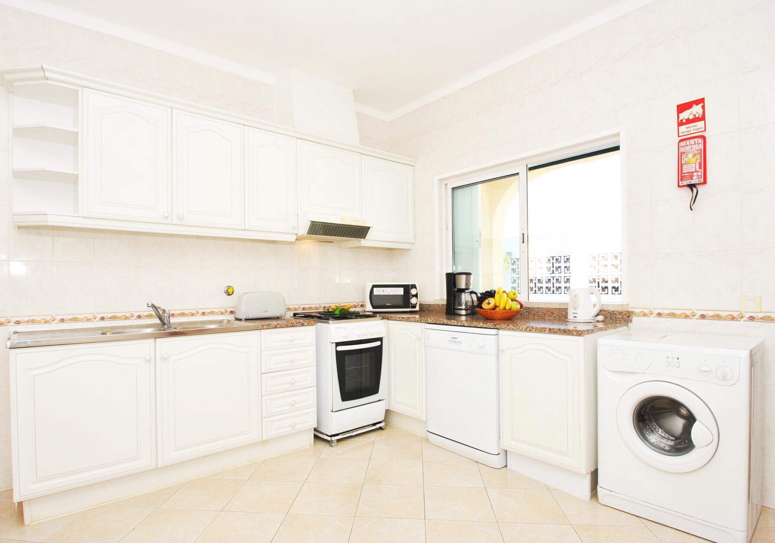 A kitchen with white cabinets, a stove, a dishwasher, a washing machine, and a coffee maker.