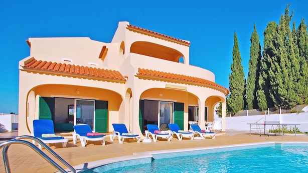 A two-story building with a swimming pool, blue lounge chairs, and a clear blue sky. - Traditional villa with BBQ and heatable pool (Albufeira)
