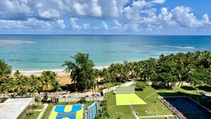 A beach view with a tennis court and palm trees. - Caribbean Beach front King bed with large balcony (Luquillo)