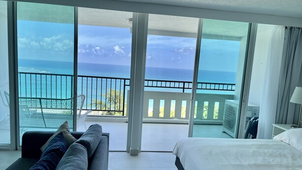 A hotel room with a large balcony, a bed, a sofa, and a view of the ocean. - Caribbean Beach front King bed with large balcony (Luquillo)