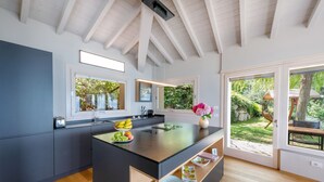 A modern kitchen with a central island, wooden flooring, and large windows offering views of the garden. - Luxury Villa Vela (Torri del Benaco)