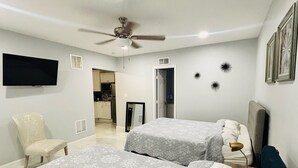 Un dormitorio con dos camas, ventilador de techo, televisor y una silla.