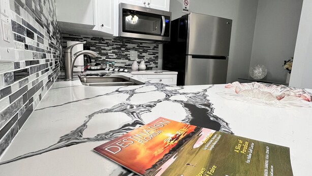 Una cocina moderna con gabinetes blancos, un refrigerador de acero inoxidable y un microondas. Un libro titulado 'Destination Florida' está sobre la encimera.