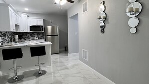 Una cocina moderna con armarios blancos, un refrigerador de acero inoxidable y una barra con dos taburetes.