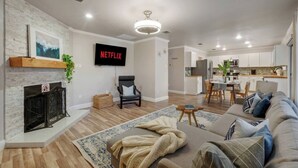 Un salon moderne avec une cheminée, un canapé, un téléviseur et une cuisine en arrière-plan.