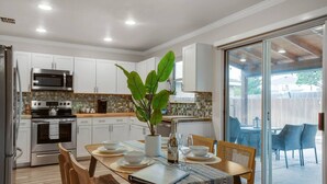 Une cuisine moderne avec des armoires blanches, des appareils en acier inoxydable et un coin repas avec une table dressée pour quatre personnes.