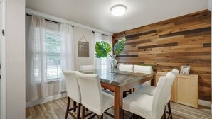 Un coin repas avec un mur en bois, des rideaux blancs et une table entourée de chaises.