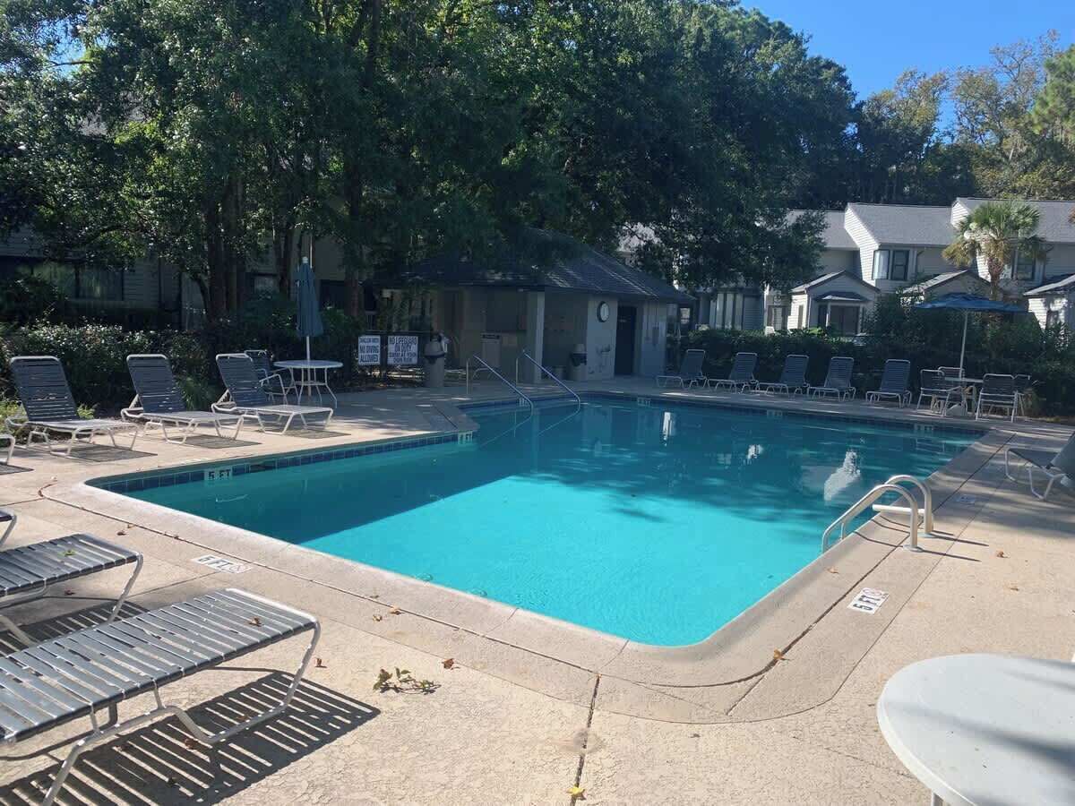 A rectangular swimming pool with a tiled deck, surrounded by lounge chairs and a small building.