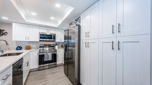 A modern kitchen with white cabinets, stainless steel appliances, and a wooden floor. - 🌴HEATED POOL AND JACUZZI FOR YEAR ROUND RELAXATION ON OCEAN FRONT BEACH⛱️ 
 (Indian Shores)