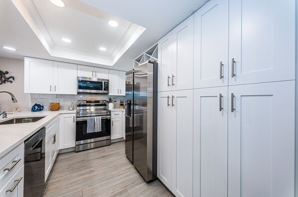 A modern kitchen with white cabinets, stainless steel appliances, and a wooden floor.