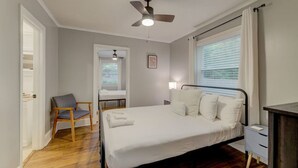Een slaapkamer met een bed, een stoel, een nachtkastje, een plafondventilator en een raam met gordijnen.
