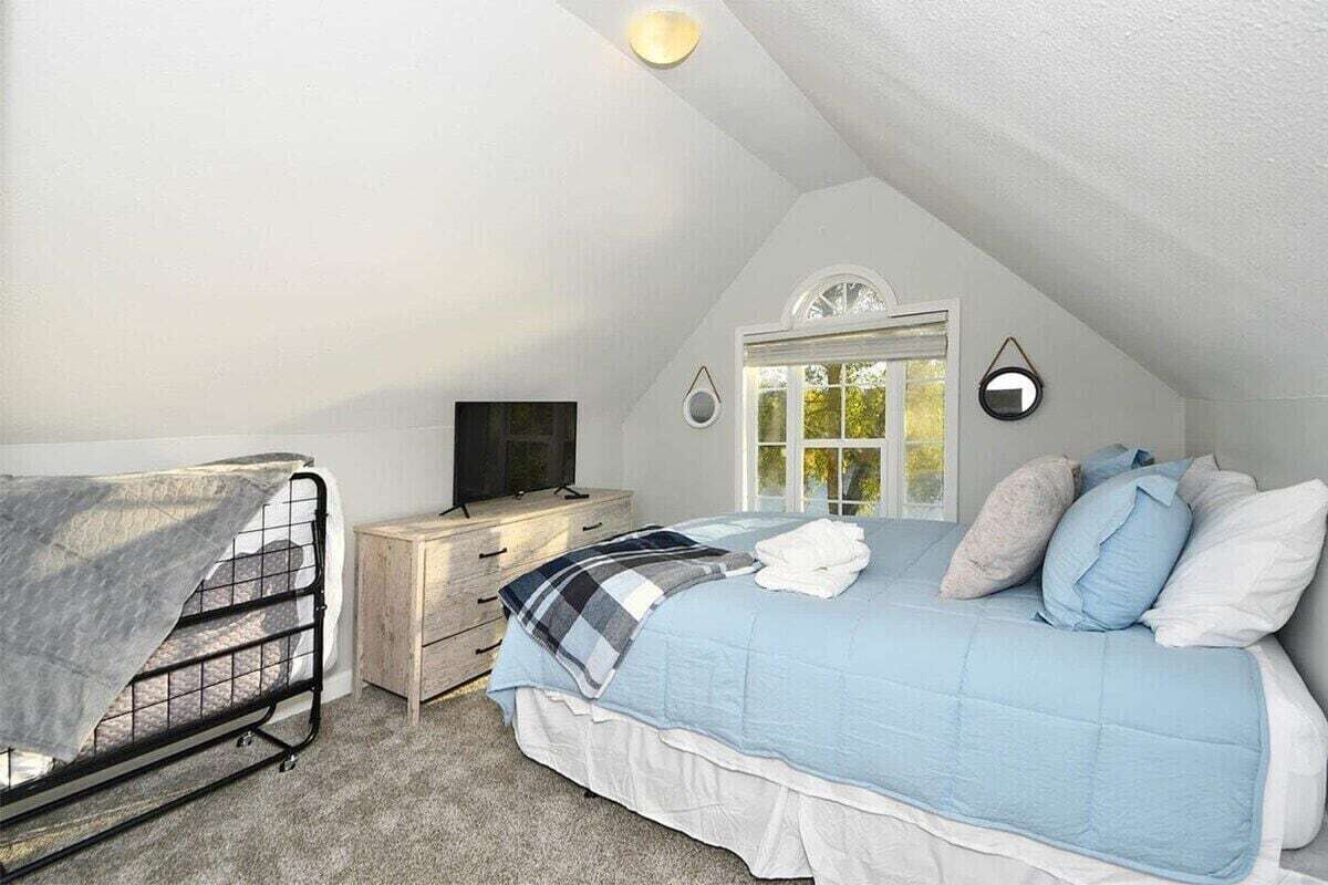 Et soveværelse med seng, natbord, fjernsyn og et vindue.