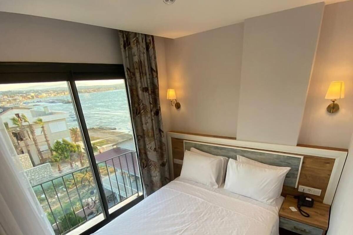 A hotel room with a large bed, a nightstand, a lamp, a ceiling light, and a view of the ocean.