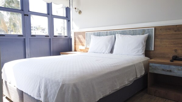 A bedroom with a large bed, a wooden headboard, a nightstand, and a window with blinds. - Houdini Otel (Urla)