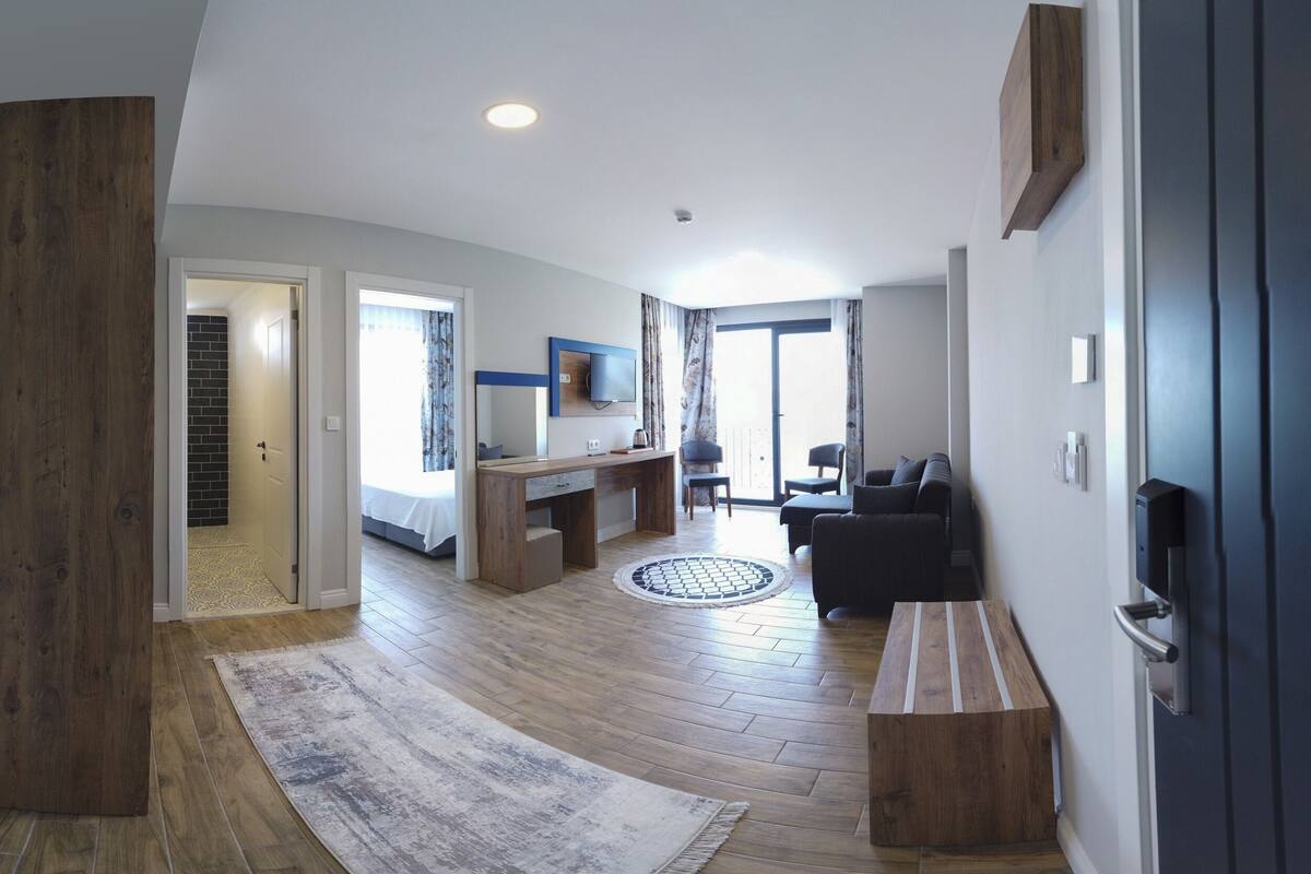 A spacious living area with a wooden floor, a round rug, a dark sofa, and a flat-screen TV mounted on the wall.