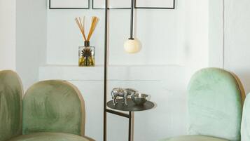 Une pièce comprenant deux fauteuils verts, un lampadaire, une petite table avec un chandelier et trois tableaux encadrés accrochés au mur.