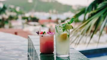 Two cocktails on a table with a pool and mountains in the background.