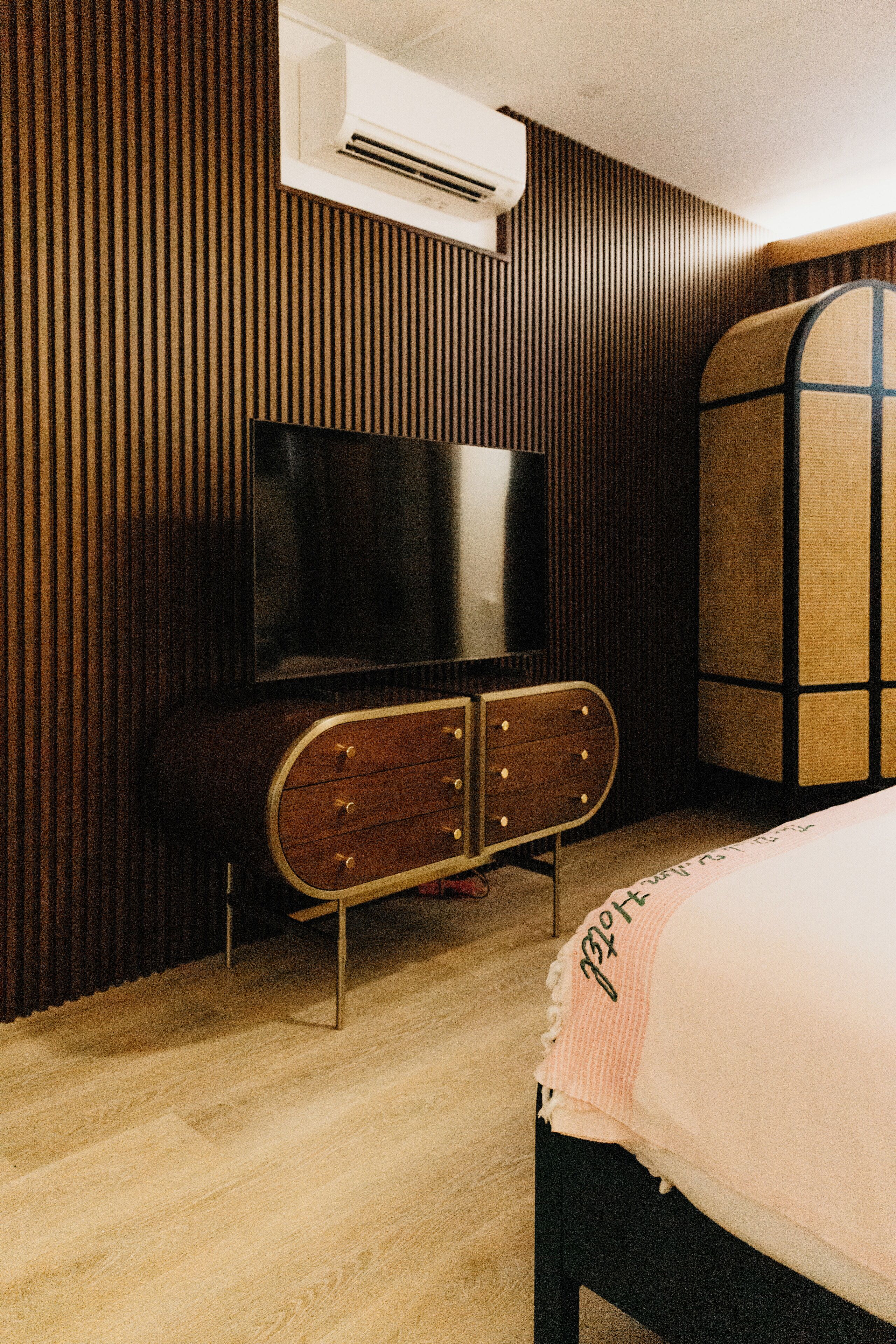 Ein Zimmer mit Holzwand, Flachbildfernseher, Holzkommode und Bett mit weißer Decke.