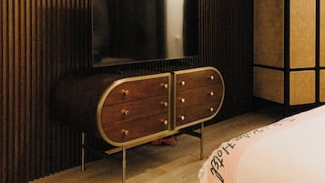 Ein Zimmer mit Holzwand, Flachbildfernseher, Holzkommode und Bett mit weißer Decke.