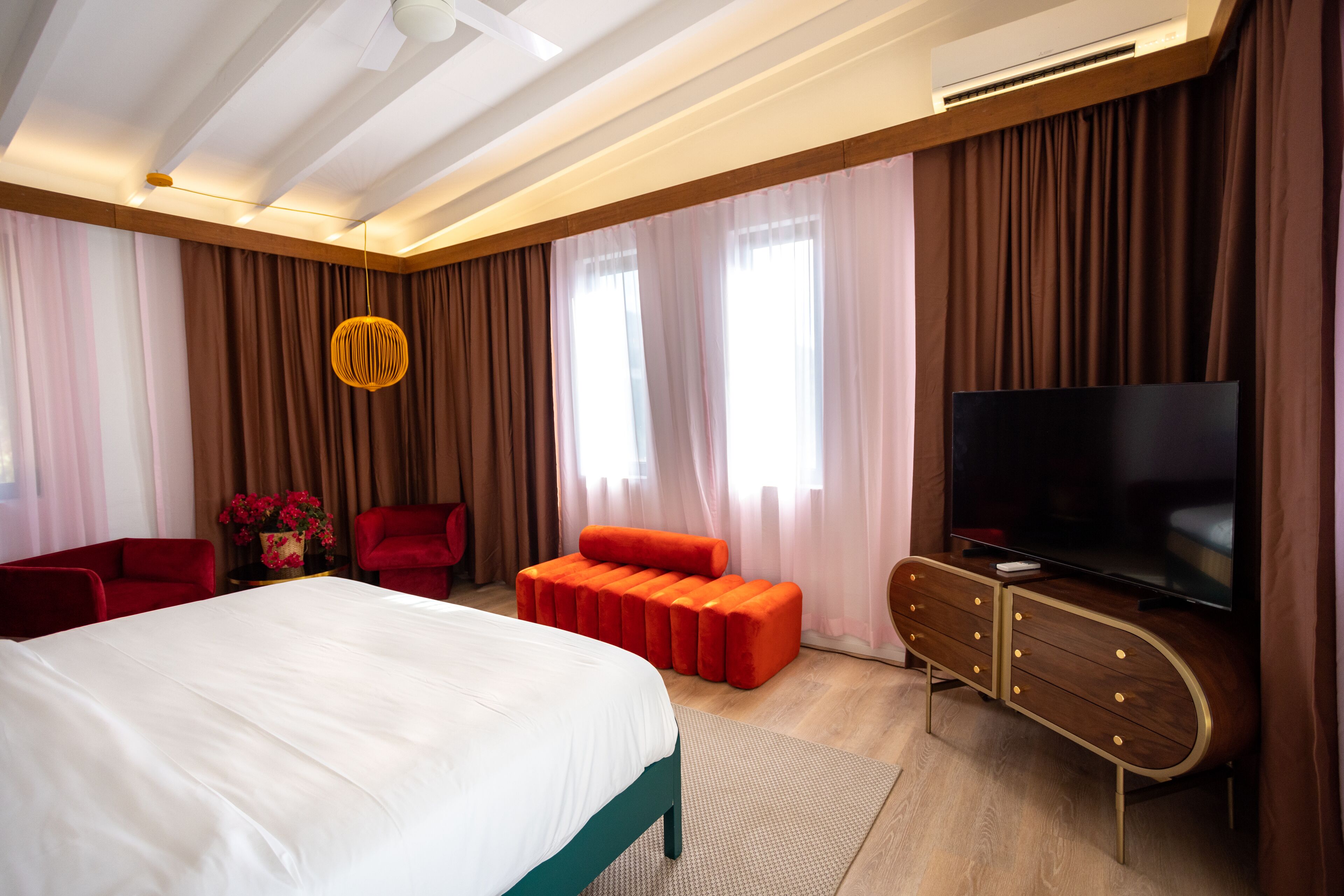 Ein modernes Hotelzimmer mit einem großen Bett, einem Fernseher, einem roten Sofa und einem Holzschrank.