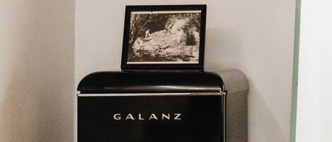 Un réfrigérateur Galanz noir, orné d’une image sur le dessus, deux chaises roses et une table avec un set de table blanc et jaune.