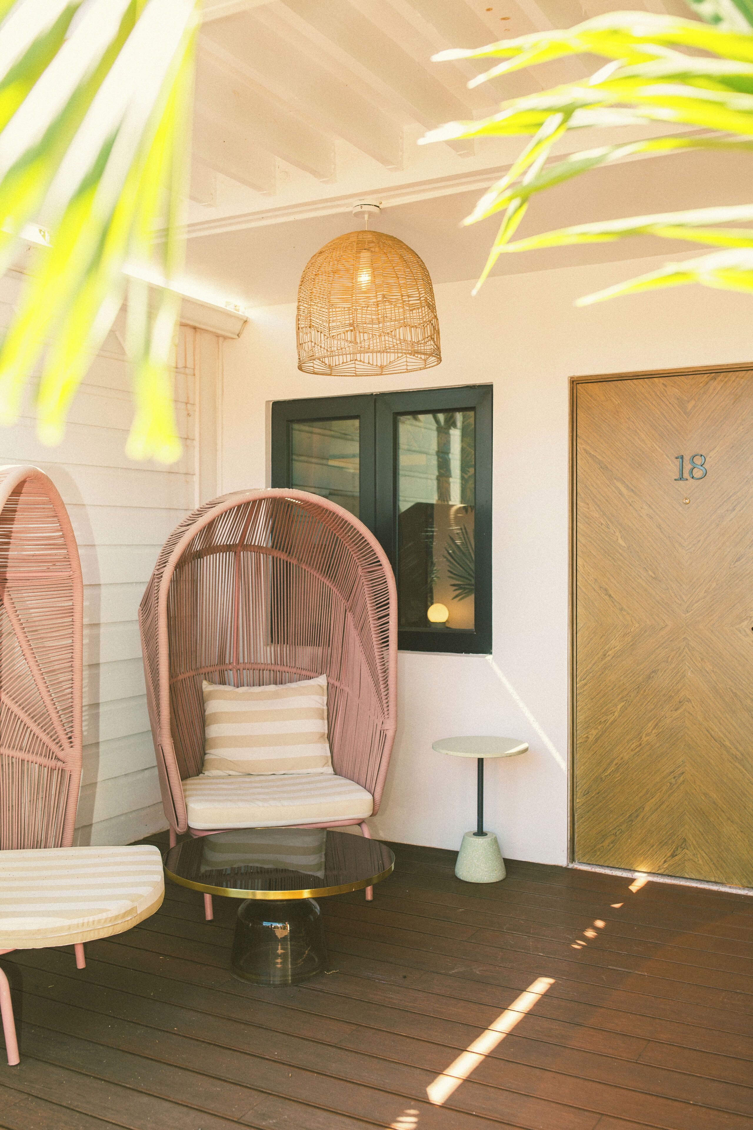 A wooden deck with wicker chairs and a table, a hanging light fixture, a framed picture, and a door with the number 18.