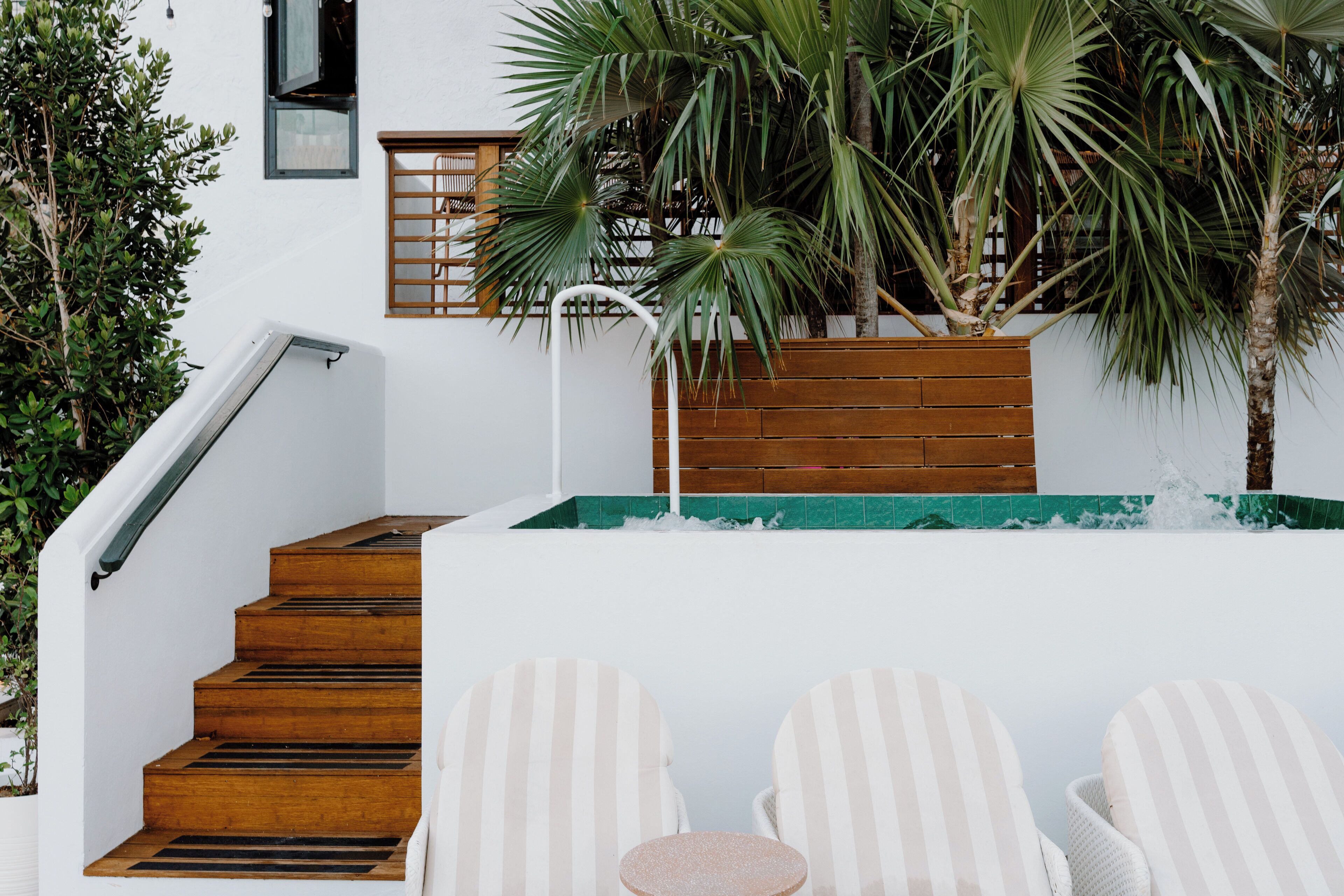 Een moderne buitenruimte met een houten trap, een kleine ronde tafel en twee gestreepte lounge fauteuils.