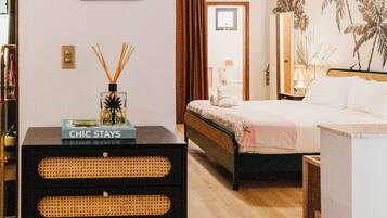 A hotel room with a bed, a dresser, a mirror, a plant, and a wall-mounted picture.