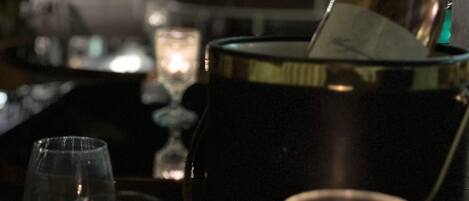 A bar setting with a bottle of champagne, two glasses of wine, and a candle on a table.