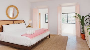 A bedroom with a bed, a mirror, a nightstand, a potted plant, and a view of the outdoors.