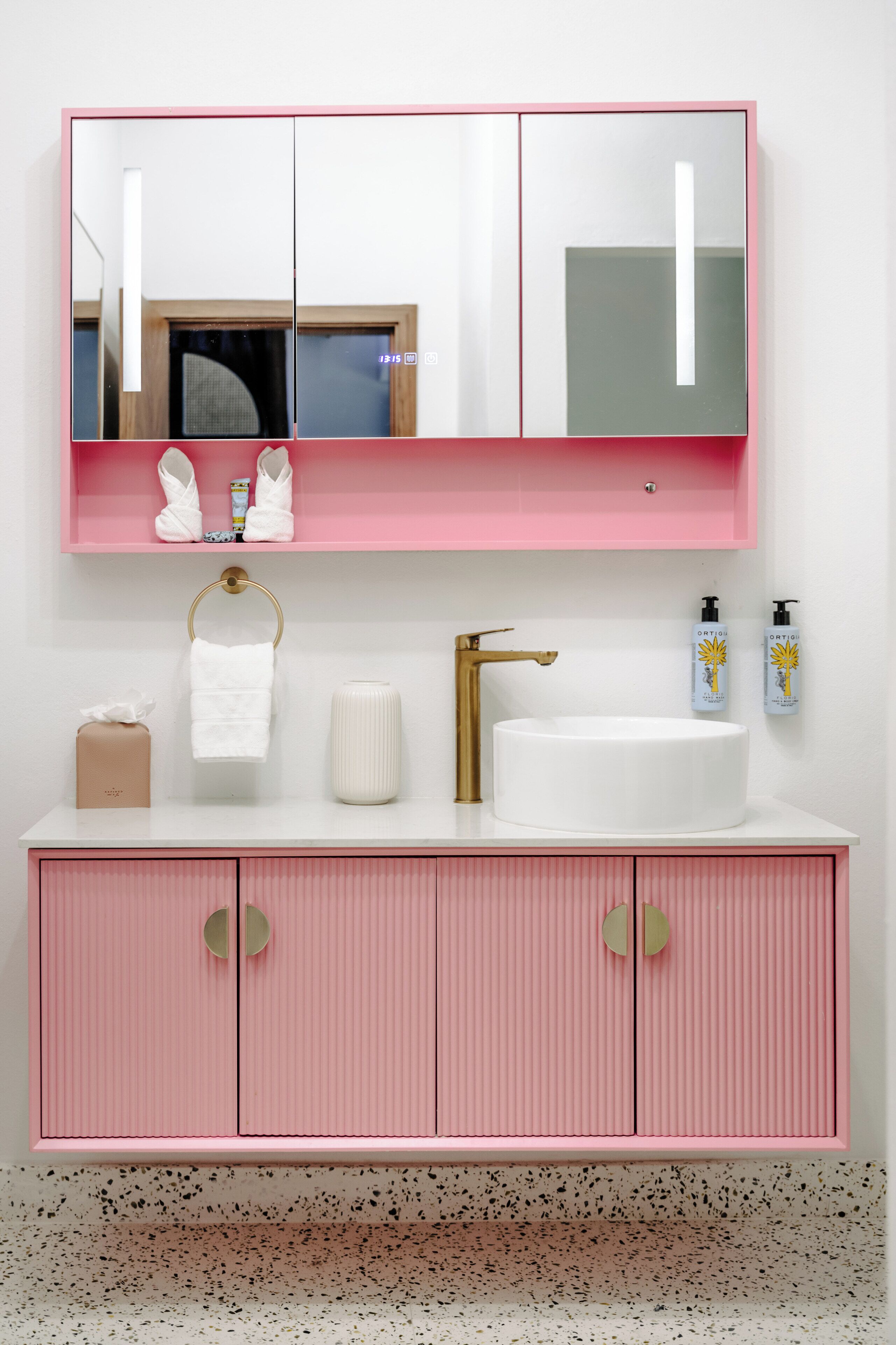 Une salle de bain avec un meuble-lavabo rose, un lavabo blanc et un miroir au-dessus.