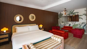 Quarto de hotel com cama grande, ventoinha no teto, sofá vermelho e um mural na parede.