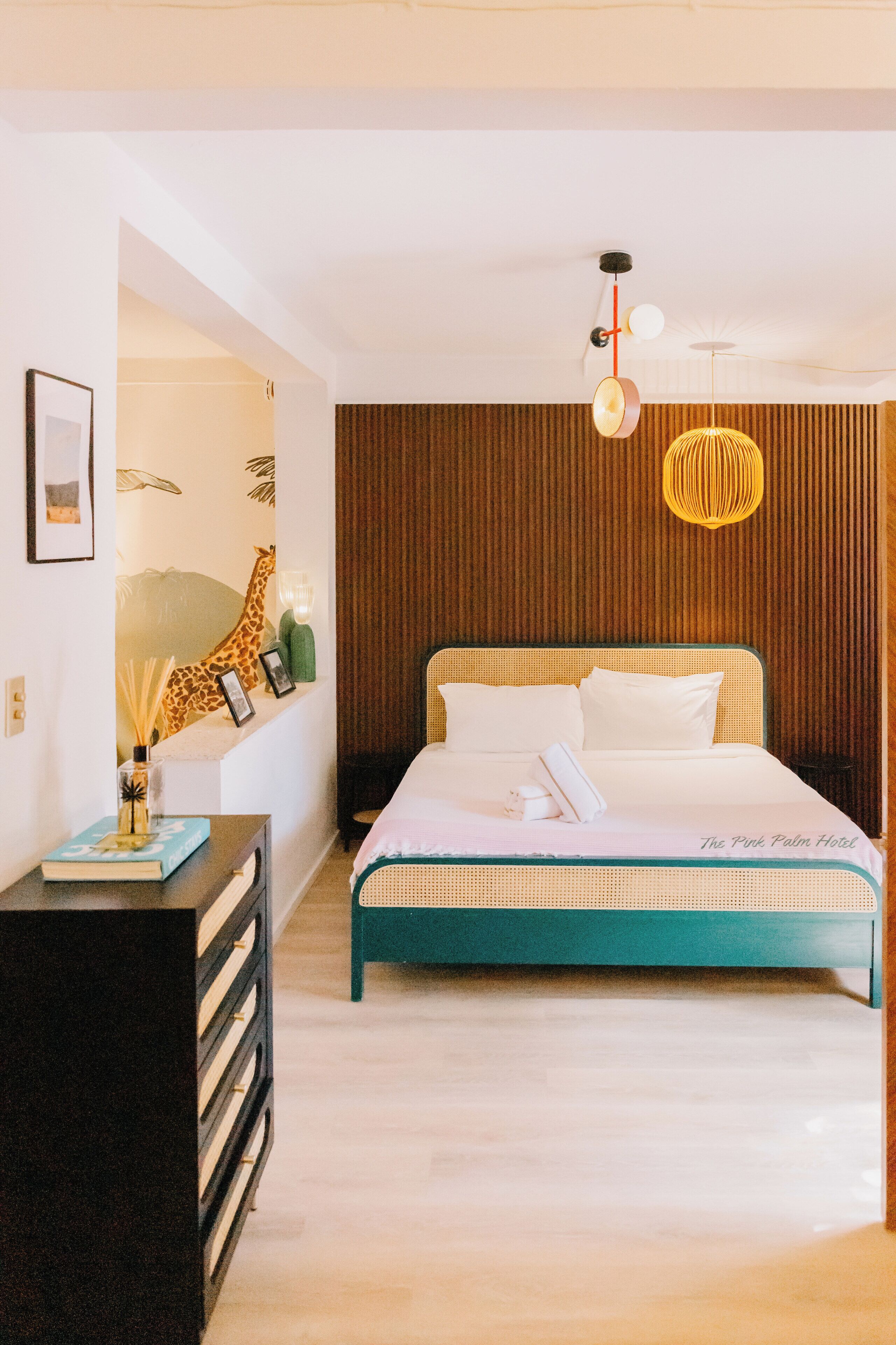 A modern hotel room with a large bed, a nightstand, a wall-mounted shelf with decorative items, and a unique ceiling light fixture.