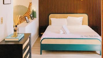 A modern hotel room with a large bed, a nightstand, a wall-mounted shelf with decorative items, and a unique ceiling light fixture.