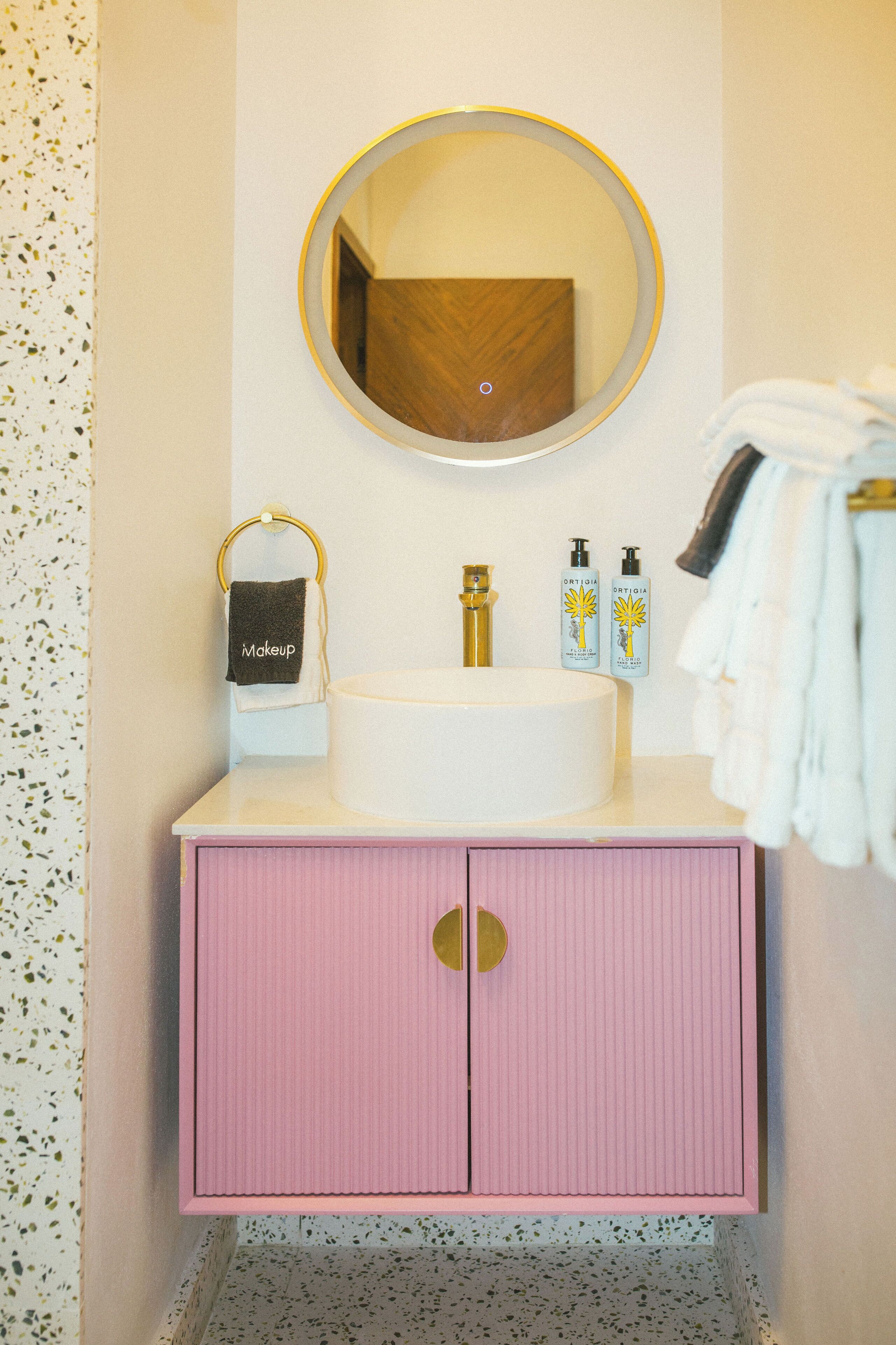A bathroom with a round mirror, a sink, and a pink cabinet.
