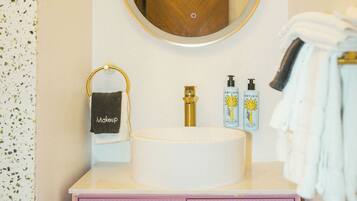 A bathroom with a round mirror, a sink, and a pink cabinet.