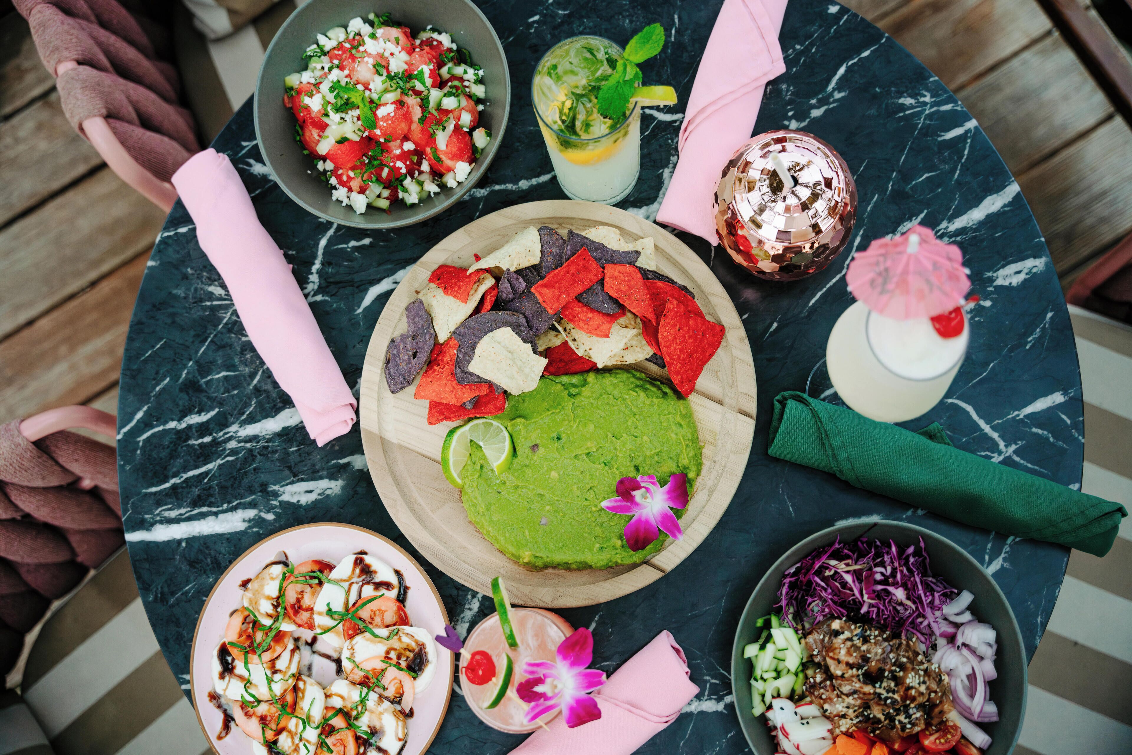 Een tafel met verschillende gerechten, waaronder groene guacamole, een salade en een bord gamba's.