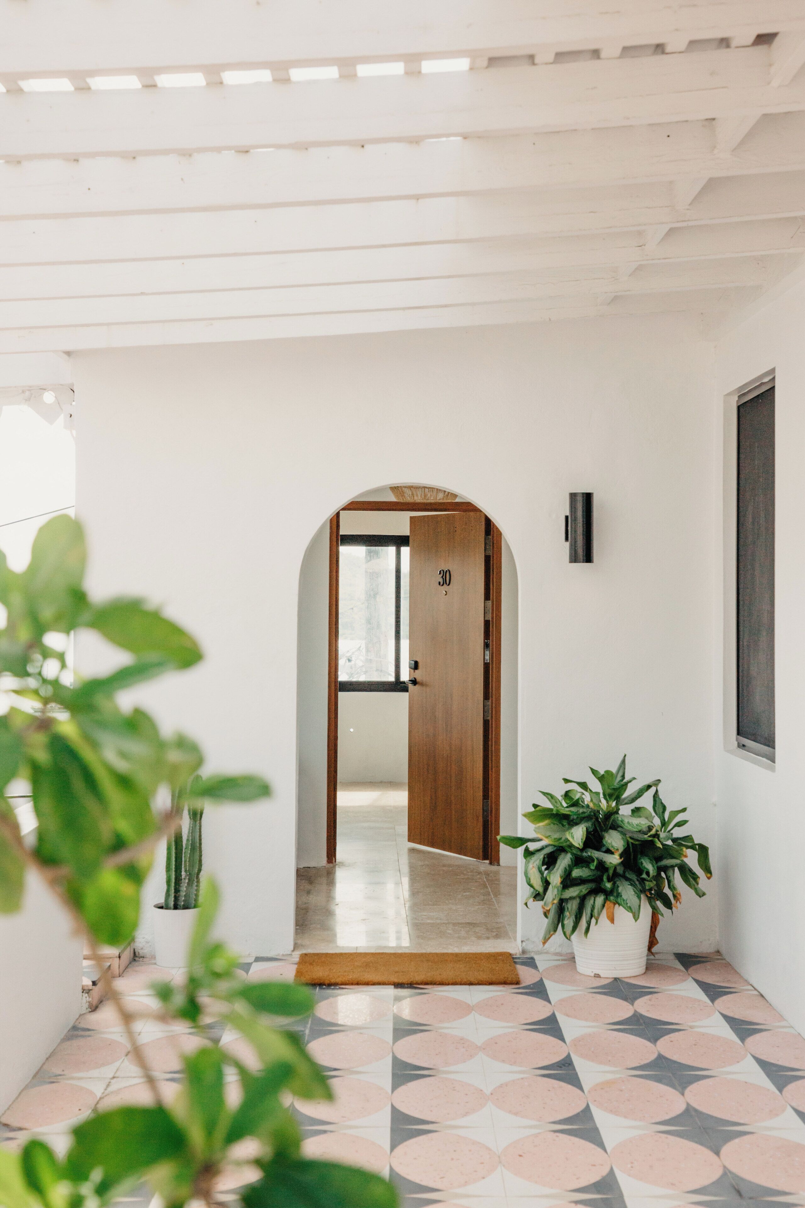 A hallway with a wooden door labeled "30", a potted plant, and a tiled floor with a geometric pattern.
