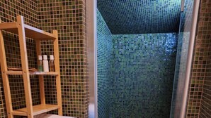 Un espace douche doté d’une étagère en bois pour les serviettes, d’une porte en verre et d’un sol carrelé.