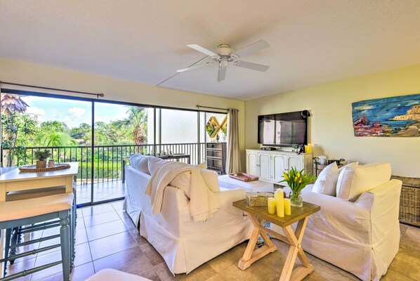 A spacious living area with a balcony, a ceiling fan, a sofa set, a small table with candles, and a television. - Comfortable Siesta Key Condo w/ Pool Access! (Siesta Key)