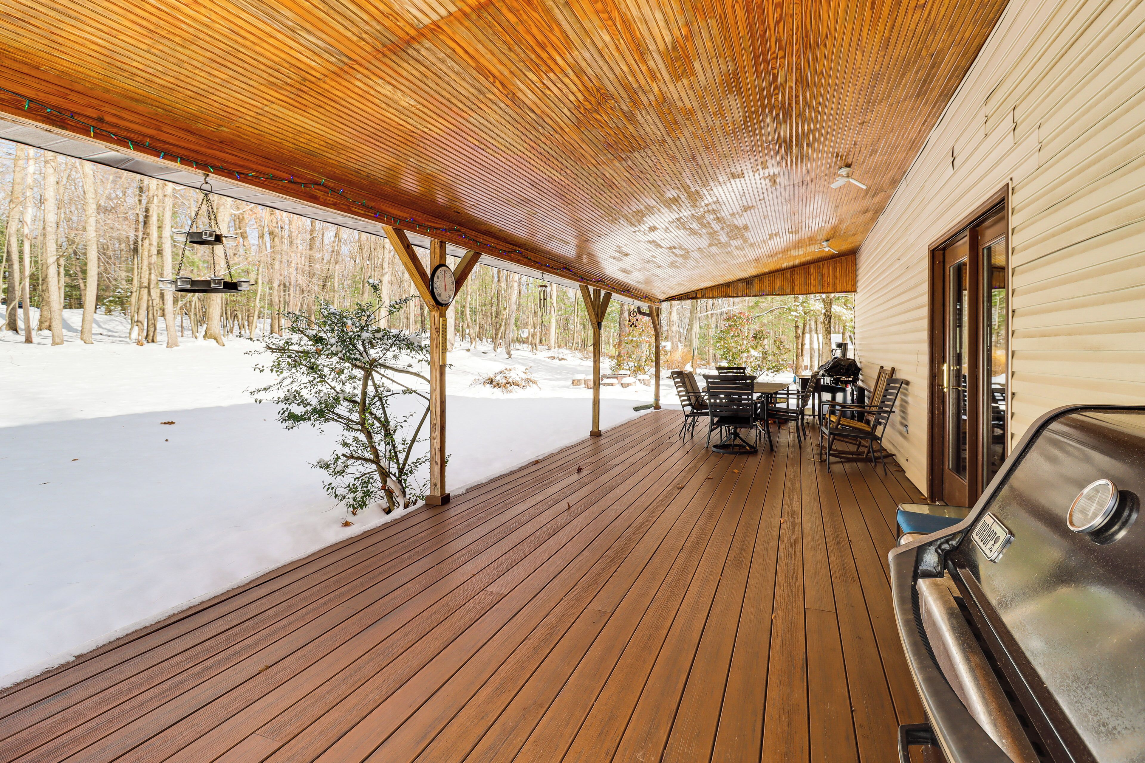 A covered wooden deck with a grill and outdoor seating area, overlooking a snowy landscape.