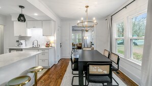 A modern kitchen with white cabinetry, a central island with stools, and a dining area with a long table and chairs. - Location!! - The Davidson - Charming Home in Fayetteville Historic District (Fayetteville)