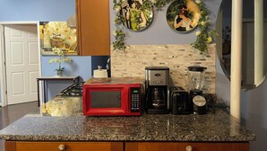 Una cocina con encimera de granito, un microondas rojo, una cafetera Cuisinart, una licuadora y un salpicadero con diseño de mosaico.