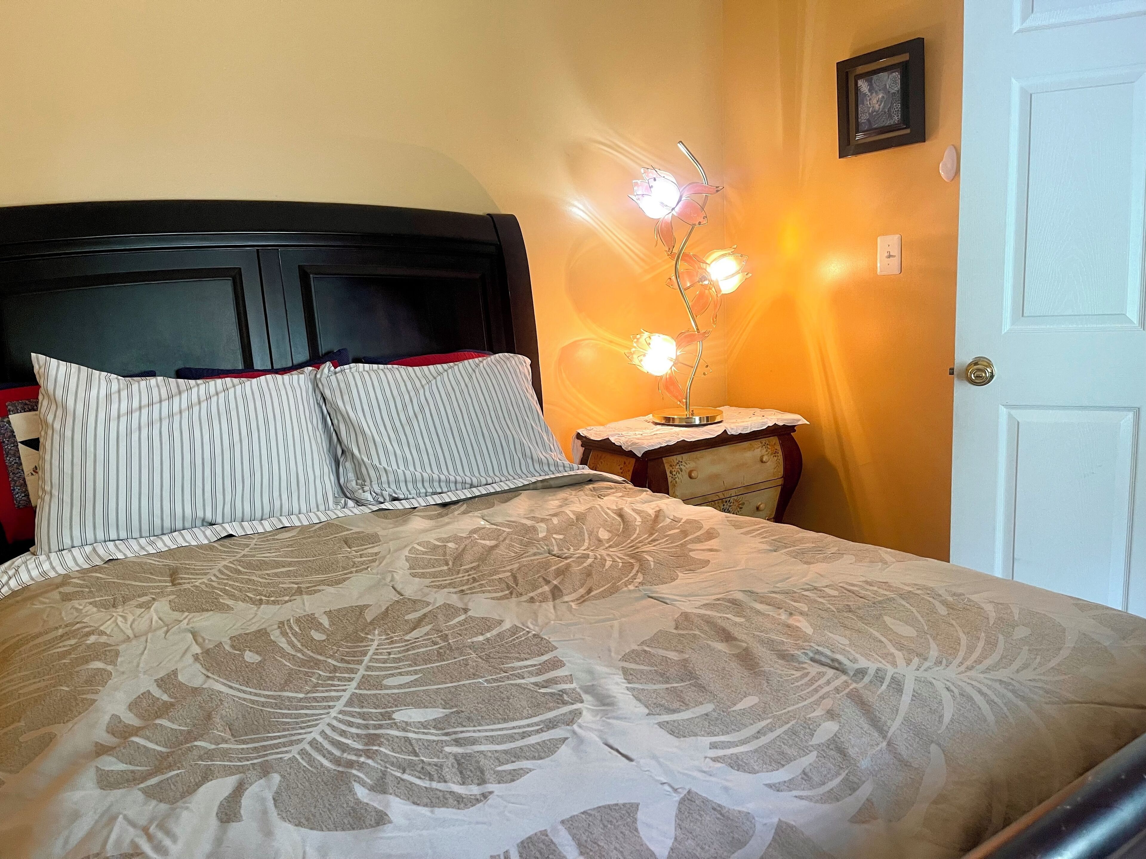 A bed with a floral-patterned bedspread, two striped pillows, and a nightstand with a lamp.