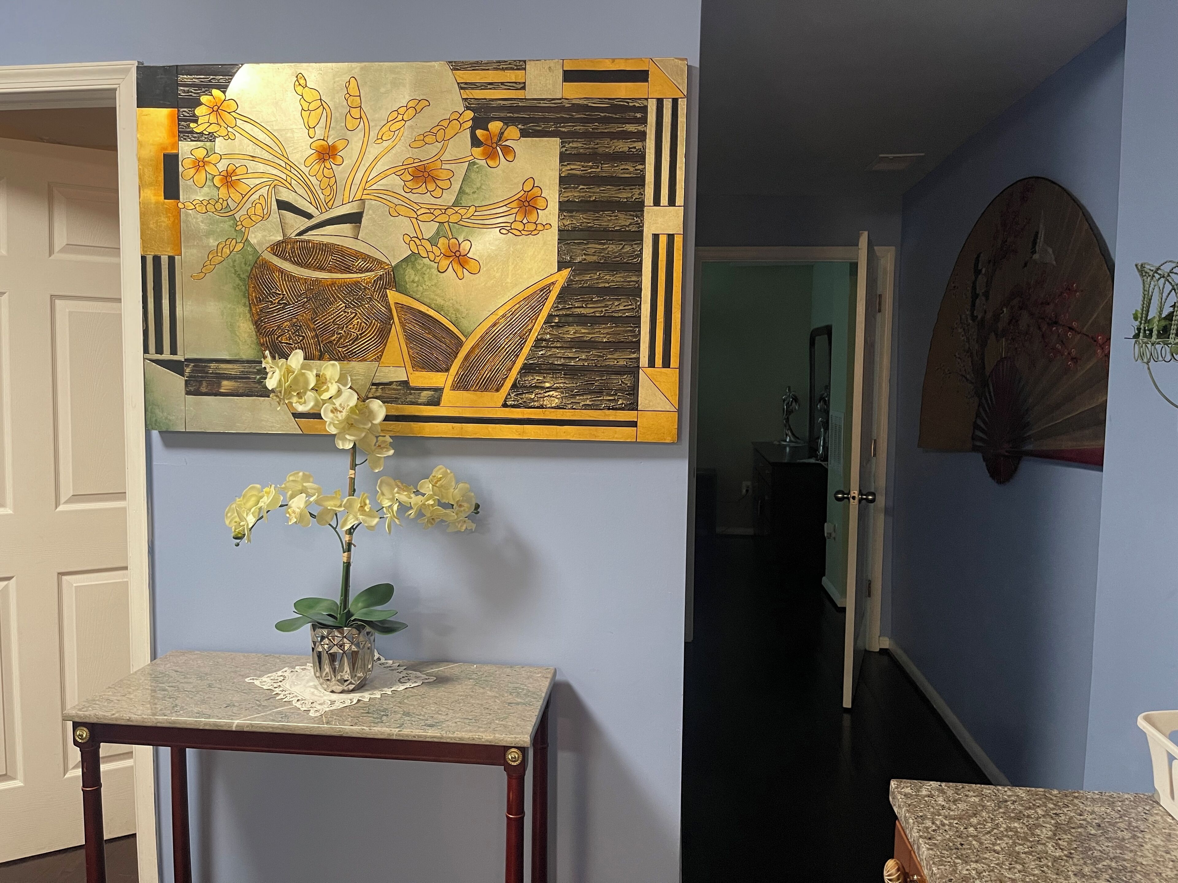 A hallway with a decorative wall piece, a small table with a vase of flowers, and a door leading to another room.