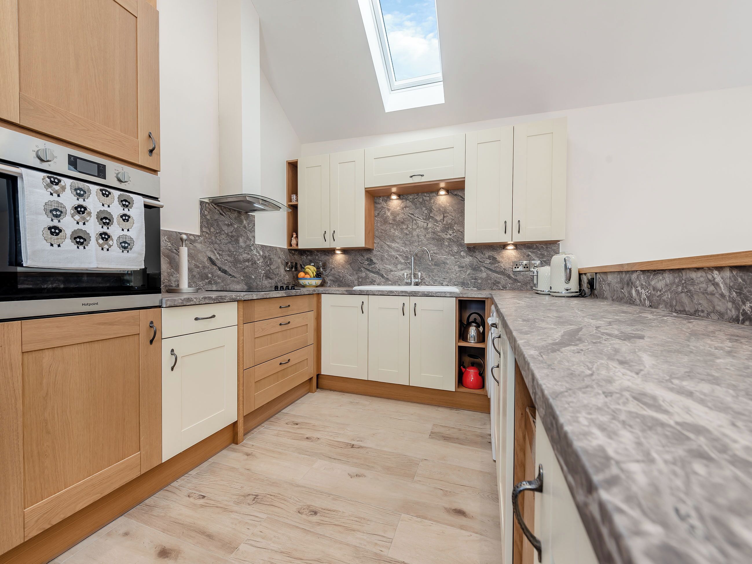 A modern kitchen with wooden cabinets, a built-in oven, a marble backsplash, and a skylight.